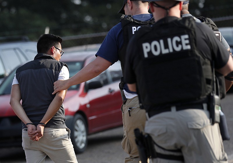 In this Aug. 7, 2019, file photo, a man is taken into custody at a Koch Foods Inc. plant in Morton, Miss. Unauthorized workers are jailed or deported, while the managers and business owners who profit from their labor often aren't. Under President Donald Trump, the numbers of owners and managers facing criminal charges for employing unauthorized workers have stayed almost the same. (AP Photo/Rogelio V. Solis, File)