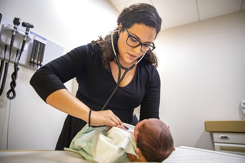 In this Tuesday, Aug. 13, 2019, photo, Dr. Jasmine Saavedra, a pediatrician at Esperanza Health Centers whose parents emigrated from Mexico in the 1980s, examines Alondra Marquez, a newborn baby in her clinic in Chicago. Doctors and public health experts warn of poor health outcomes and rising costs they say will come from sweeping changes that would deny green cards to many immigrants who use Medicaid, as well as food stamps and other forms of public assistance. Saavedra is convinced that if new Trump administration criteria were in effect for her parents three decades ago, she wouldn't have become a pediatrician.