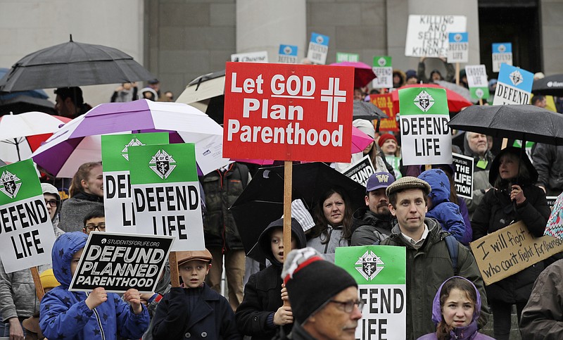 FILE - In this Jan. 22, 2019, file photo, people taking part in an anti-abortion march hold signs as they stand on the steps of the Legislative building at the Capitol in Olympia, Wash. With a flurry of recent actions, Trump's administration is now winning the praise of conservative religious leaders for fulfilling many of their goals opposing abortion and reining in the LGBTQ-rights movement. (AP Photo/Ted S. Warren, File)