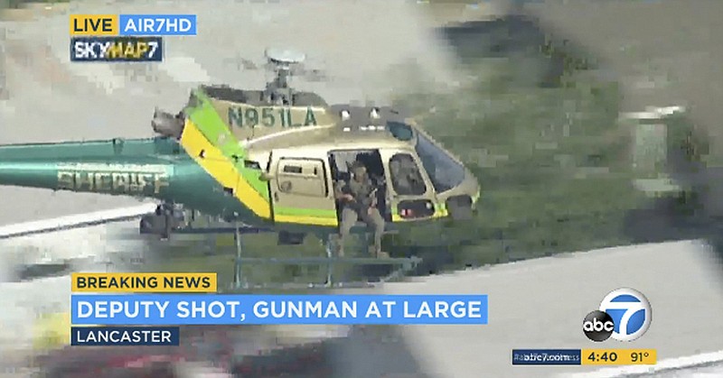 This photo taken from video provided by KABC-TV shows a sheriff's department helicopter with a sniper in an open door searching for a gunman at large in Lancaster, Calif. on Wednesday, Aug. 21, 2019. The mayor of Lancaster says a deputy shot and wounded outside a Los Angeles County sheriff's station is going to be okay after visiting him in the hospital. Authorities are searching for the shooter in buildings surrounding the station where the deputy was hit in the shoulder while standing in the parking lot Wednesday afternoon. (KABC-TV via AP)