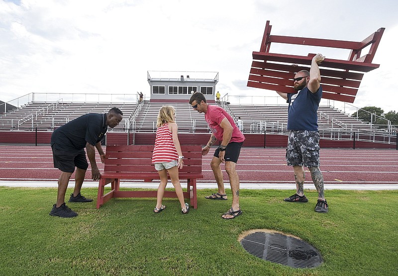 Jerry Careathers, left, and Howard construction teacher Zack Vice place one sideline bench as welding teacher Mitch Williams hoists another over his head Friday before the opening game at the school's White Field. Tsali Vice, 7, Zack's daughter, helps out.