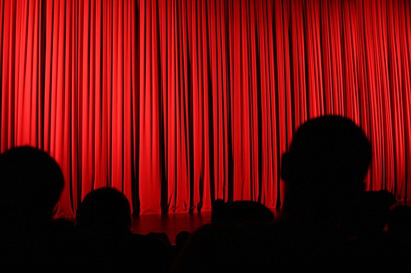 An audience facing the stage during an intermission with the curtains drawn.
theater tile red curtain tile / Getty Images