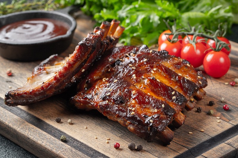 Closeup of pork ribs grilled with BBQ sauce and caramelized in honey. Tasty snack to beer on a wooden Board for filing on dark concrete background. ribs tile food / Getty Images
