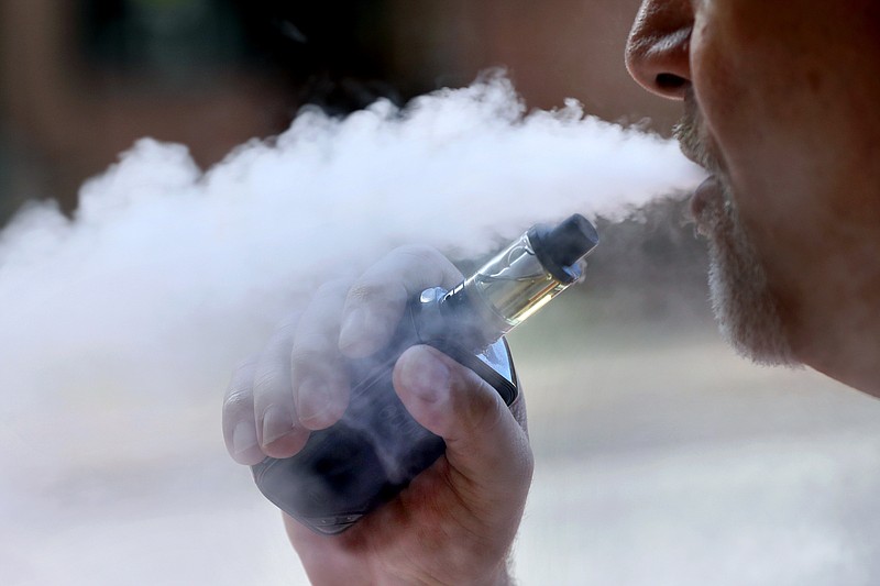 In this Aug. 28, 2019, file photo, a man exhales while smoking an e-cigarette in Portland, Maine. Oregon's public health physician said Wednesday, Sept. 4, 2019, that a person who contracted a severe respiratory illness and died after using an e-cigarette had purchased a vaping device containing marijuana oil at a state-legal dispensary. The death is the second linked by public health officials nationwide to vaping and the first linked to an e-cigarette purchased at a dispensary. (AP Photo/Robert F. Bukaty, File)
