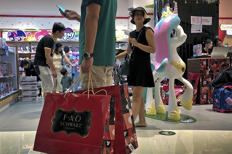 In this June 1, 2019, photo, file a man carries a paper bags containing toys purchased from the FAO Schwarz as people shop at the newly open FAO Schwarz toy store at the capital city's popular shopping mall in Beijing. Caught in the crossfire of a trade war, American businesses operating in the China say they've been hurt by the hostilities between the world's two biggest economies and are facing increasingly unfair competition from Chinese firms. (AP Photo/Andy Wong, File)