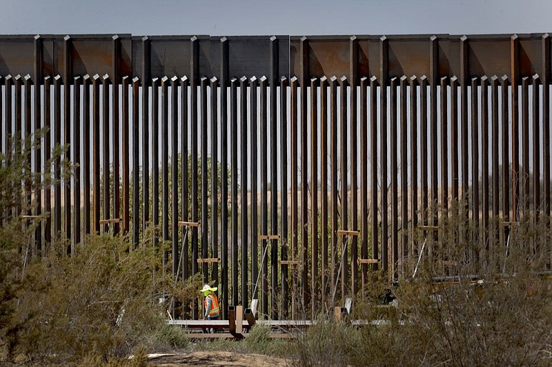 A government contractor walks beside a completed section of Pentagon-funded border wall along the Colorado River, Tuesday, Sept. 10, 2019 in Yuma, Ariz. The 30-foot high wall replaces a five-mile section of Normandy barrier and post-n-beam fencing along the the International border that separates Mexico and the United States. Construction began as federal officials revealed a list of Defense Department projects to be cut to pay for President Donald Trump's wall. (AP Photo/Matt York)