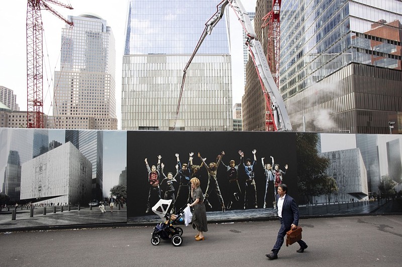 People walk by murals promoting the future site of the Ronald O. Perelman Performing Arts Center as cranes work over the site at the World Trade Center, Monday, Sept. 9, 2019 in New York. The arts building is one of the final pieces to be completed as part of the reconstruction of the World Trade Center. Wednesday marks the 18th anniversary of the attacks of Sept. 11, 2001. (AP Photo/Mark Lennihan)


