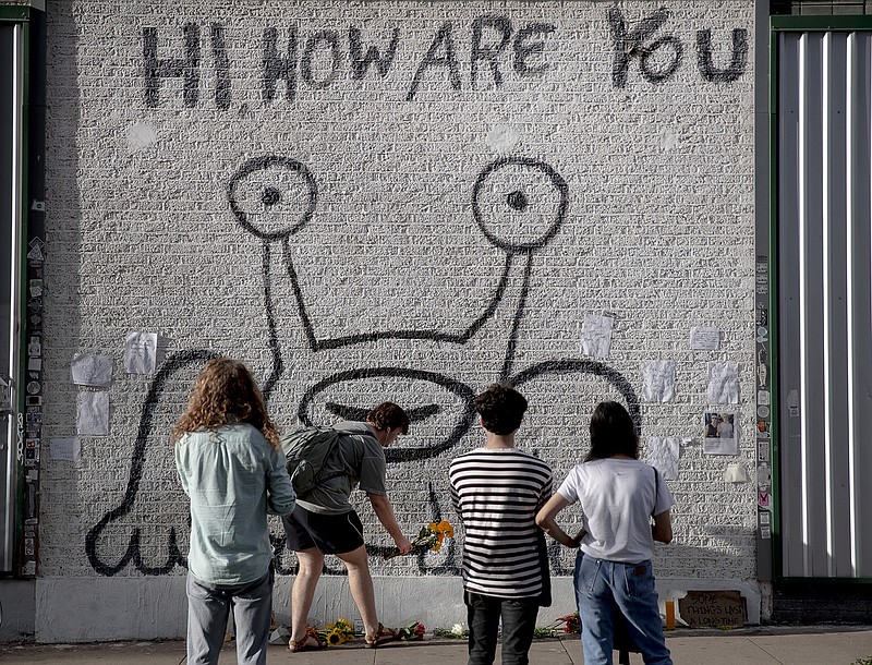 Alistair Keggen leaves flowers at the "Hi, How Are You" mural created by artist Daniel Johnston on Wednesday, Sept. 11, 2019, in Austin, Texas. Johnston, a quirky folk singer-songwriter and visual artist whose offbeat career and struggles with mental illness brought him a cult following and inspired a documentary film, has died at age 58. According to a statement issued by his family, Johnston died of natural causes Wednesday morning at his Houston-area home. (Nick Wagner/Austin American-Statesman via AP)