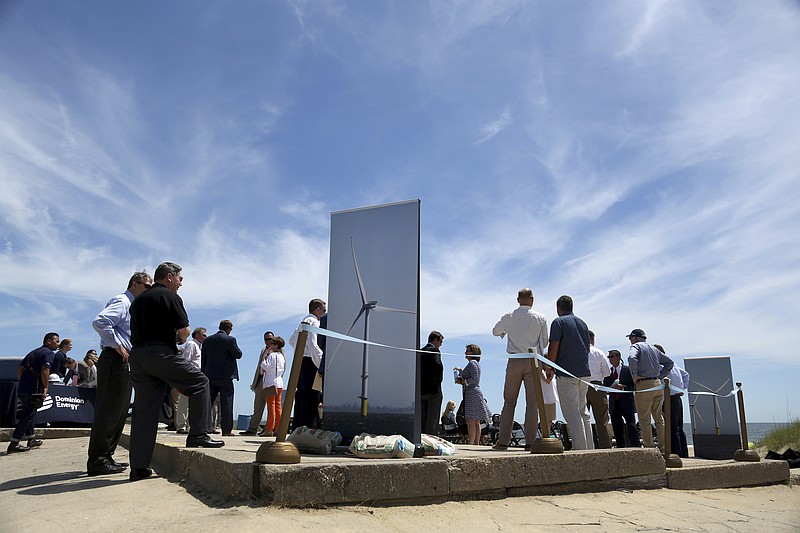 FILE - In this July 1, 2019 file photo people gather around posters of wind turbines before Dominion Energy's groundbreaking ceremony for their offshore wind turbine project at Camp Pendleton in Virginia Beach, Va. Dominion Energy announced plans Thursday, Sept. 19 to seek approval to build what it says would be the largest offshore wind project in the United States off the Virginia coast. (Sarah Holm/The Virginian-Pilot via AP, File)