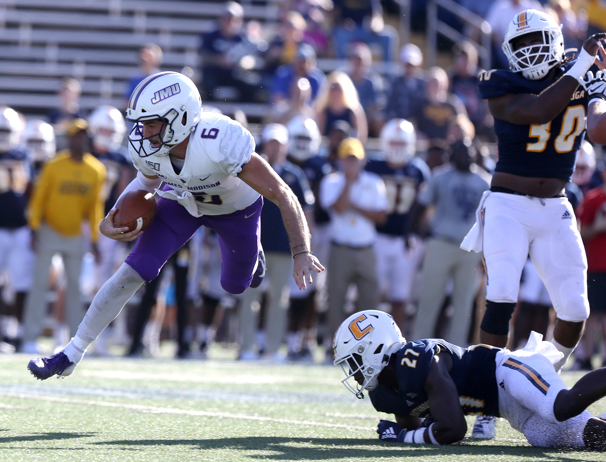 Staff photo by Erin O. Smith / James Madison University quarterback Ben DiNucci (6) is tripped up by UTC's Jerrell Lawson (27) during the UTC vs. James Madison University NCAA football game Saturday, August 21, 2019 at Finley Stadium in Chattanooga, Tennessee. JMU was up 20-14 at the half.