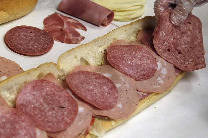 In this June 5, 2014, file photo, a man makes a submarine sandwich with mortadella, cooked salami, ham, Genoa salami and sweet capicola at a delicatessen in Massachusetts. An international team of researchers is questioning the advice to limit red and processed meats, saying the link to cancer and heart disease is weak. Their conclusions were swiftly attacked by a group of prominent U.S. scientists who tried to stop publication of the research, arguing it sends the wrong message. (AP Photo/Elise Amendola, File)