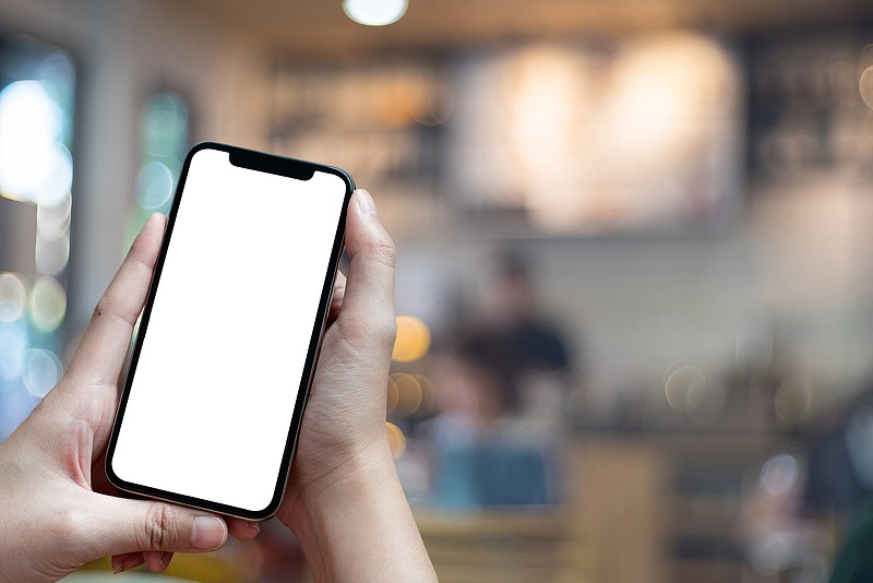 Mockup image of hand holding mobile phone with blank white Full screen in cafe For Graphic display montage / Getty Images/iStockphoto/Natee Meepian