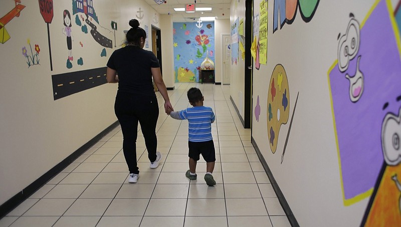 A young migrant boy walks with a Comprehensive Health Services caregiver at a "tender-age" facility, a facility for babies, children and teens, in Texas’ Rio Grande Valley, Thursday, Aug. 29, 2019, in San Benito, Texas. Sheltering migrant children is a booming business for Comprehensive Health Services, a Florida-based government contractor, as the number of children in government custody has swollen to record levels in the past two years. (AP Photo/Eric Gay)