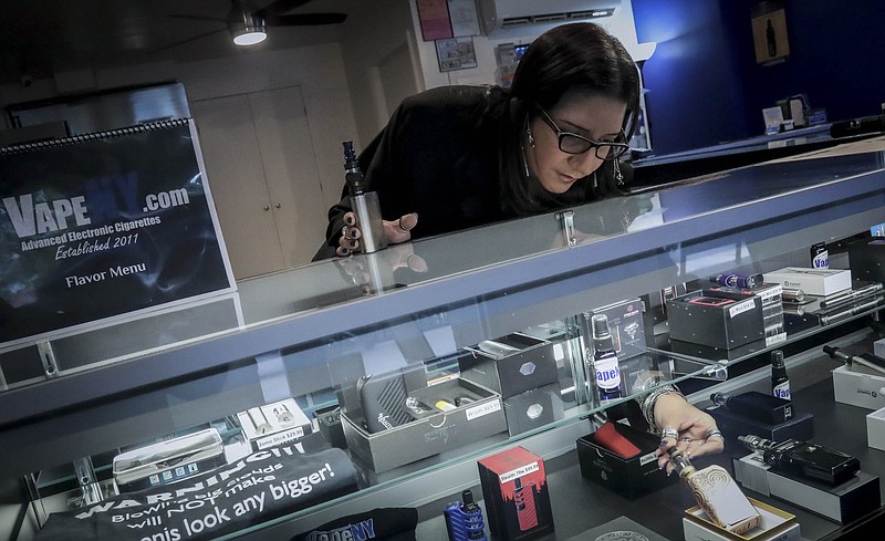 In this Tuesday, Oct. 8, 2019, photo Spike Babaian, owner of several Vape New York stores, works in her East Harlem store in New York. Sales at small businesses that sell vaping products have plunged since August, when reports of vaping-related illnesses and deaths began. “We can never undo the government going on the news and saying it’s not safe to vape. The damage has been done,” says Babaian, who has been in business for eight years.  (AP Photo/Bebeto Matthews)