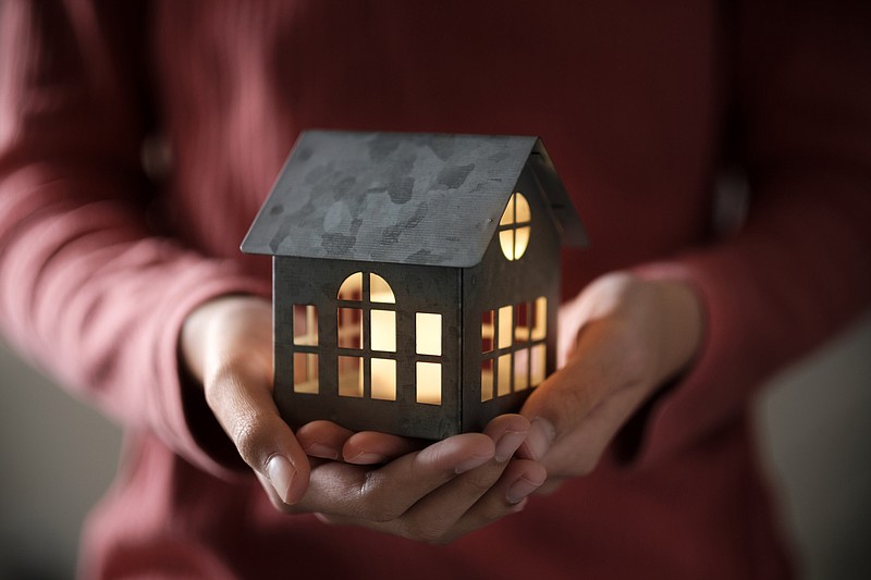 Miniature house model with illuminated light in the hand emergency shelter tile homeless tile giving charity / Getty Images
