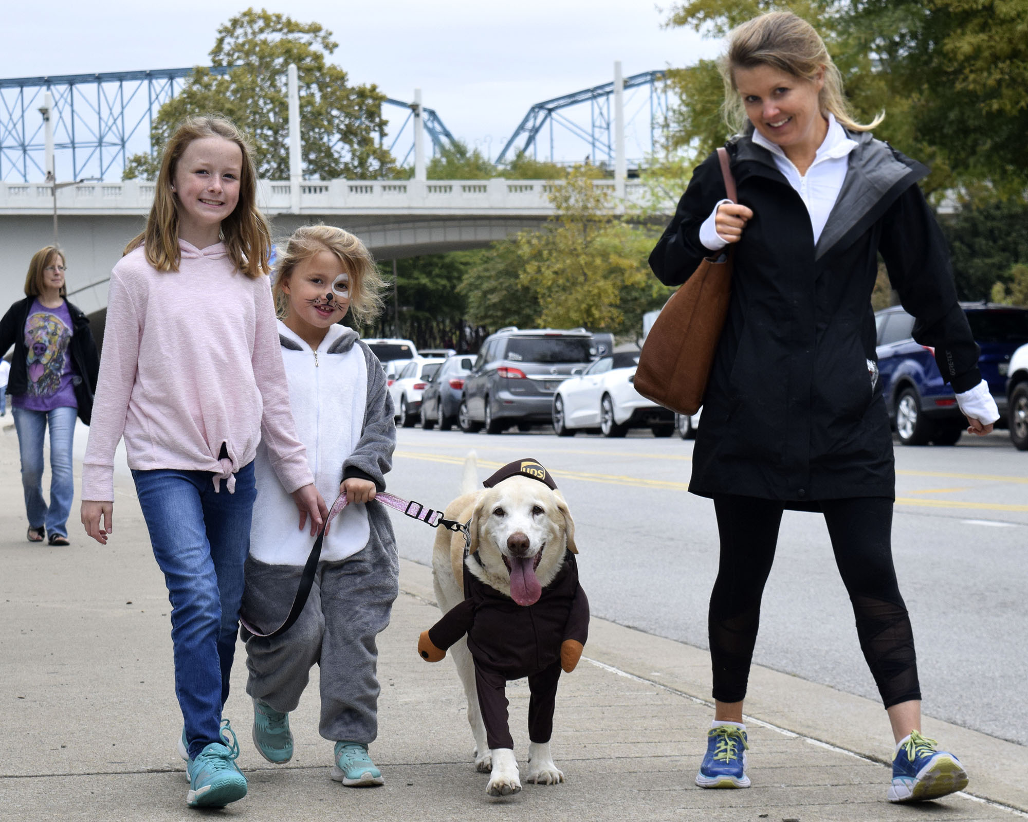 Staff Photo by Robin Rudd/ Yellow Labrador Lilly is dressed as the UPS man, while owner Caroline Estes is a huskey. Also along for the walk are Mary West Estes, left, and Maggie EstesHundreds of animals lovers gathered to raise money for the Humane Educational Society at the 17th annual Paws in the Park. The event included a walk, dog and human costume contest, and a dog cake-eating contest. Ross's Landing Park was the site of the event on October 19, 2019.