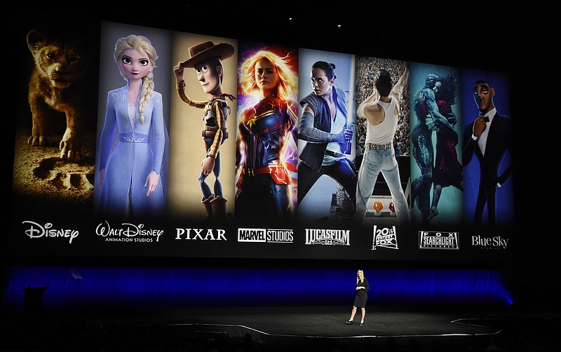 FILE - In this April 3, 2019, file photo characters from Disney and Fox movies are displayed behind Cathleen Taff, president of distribution, franchise management, business and audience insight for Walt Disney Studios during the Walt Disney Studios Motion Pictures presentation at CinemaCon 2019, the official convention of the National Association of Theatre Owners (NATO) at Caesars Palace in Las Vegas. Verizon is offering new and current customers a free year of Disney+ as the battle for streaming customers heats up. The offer extends to certain new and existing 4G and 5G customers as well as new Verizon Fios and 5G home internet customers. The promotion begins Nov. 12. (Photo by Chris Pizzello/Invision/AP, File)