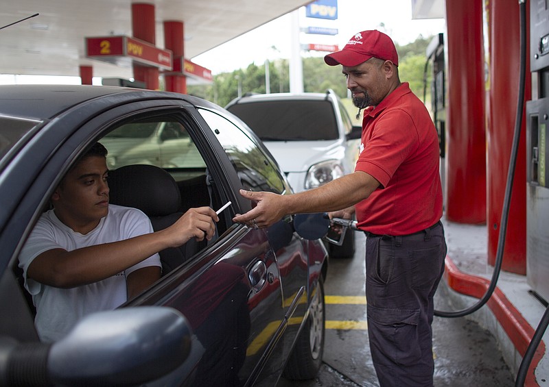 In this Oct. 8, 2019 photo, gas station attendant Leowaldo Sanchez takes a cigarette as payment from a motorist as he fills the tank in San Antonio de los Altos on the outskirts of Caracas, Venezuela. This barter system, while perhaps the envy of cash-strapped drivers outside the country, is just another symptom of bedlam in Venezuela where a full tank these days costs a tiny fraction of a U.S. penny. (AP Photo/Ariana Cubillos)