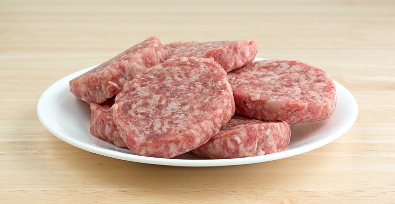 A white plate with sausage patties atop a wood counter top. / Getty Images
