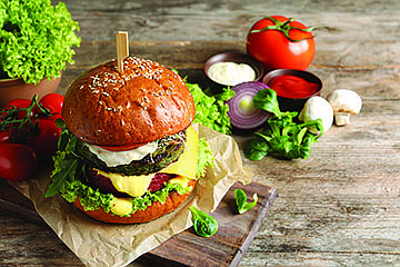 Board with vegan burger and vegetables on wooden table. Space for text