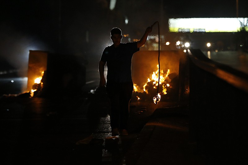 A supporter of Lebanese Prime Minister Saad Hariri burns garbage containers to block a main road in Beirut, Lebanon, Tuesday, Oct. 29, 2019. Hariri resigned Tuesday, bowing to one of the central demands of anti-government demonstrators shortly after baton-wielding Hezbollah supporters rampaged through the main protest camp in Beirut, torching tents, smashing plastic chairs and chasing away protesters. (AP Photo/Bilal Hussein)