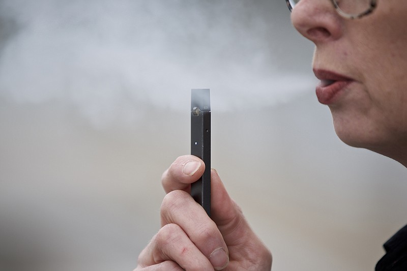 FILE - In this April 16, 2019, file photo, a woman exhales a puff of vapor from a Juul pen in Vancouver, Wash. A former Juul Labs executive is alleging that the vaping company knowingly shipped 1 million tainted nicotine pods to customers. The allegation comes in a lawsuit filed Tuesday, Oct. 29, by a former finance executive who was fired by the vaping giant earlier this year.  (AP Photo/Craig Mitchelldyer, File)