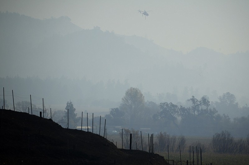 A helicopter flies though a smoky valley carrying water to fight the Kincade Fire near Healdsburg, Calif., Thursday, Oct. 31, 2019. (AP Photo/Charlie Riedel)