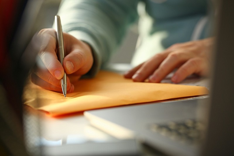 Male hand holding silver pen. Fill in address on yellow envelope of mail correspondence for application hiring concept service delivery agreement petition tile / Getty Images