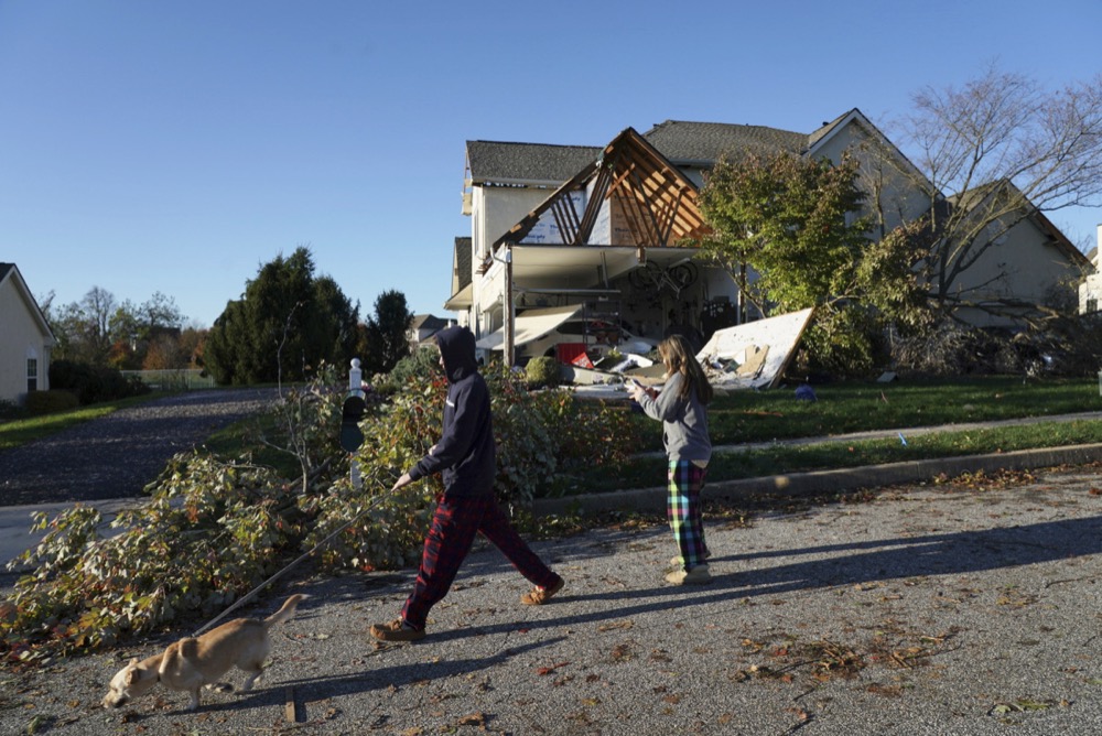 Nearby neighbors Shane wilson, left, and sister Noelle Wilson, center, walk their dog Auggie past a damaged house on Chelsea Court, in Thornbury Township, PA, where a severe storm hit the area last night, November 1, 2019. ( JESSICA GRIFFIN / The Philadelphia Inquirer via AP )