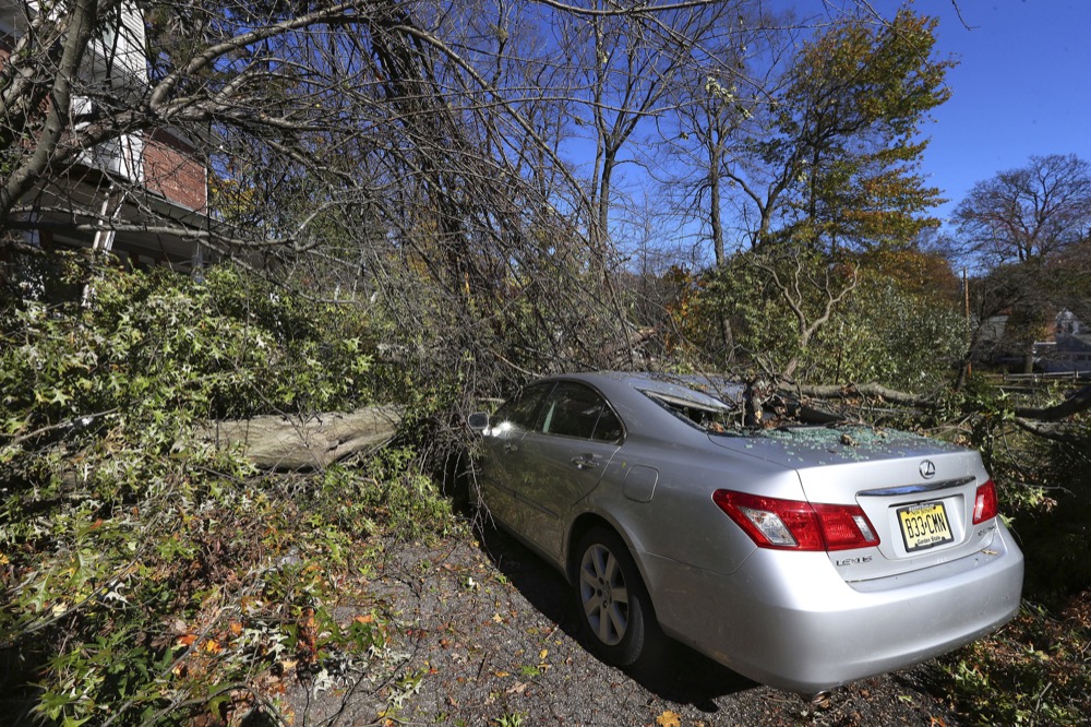 A Lexus and a front porch is crushed by an Oak tree at a house on Green Village Road on Friday, Nov. 1, 2019, in Madison, N.J. The Borough was hit be high winds on heavy rain late last night. (AP Photo/Rich Schultz)