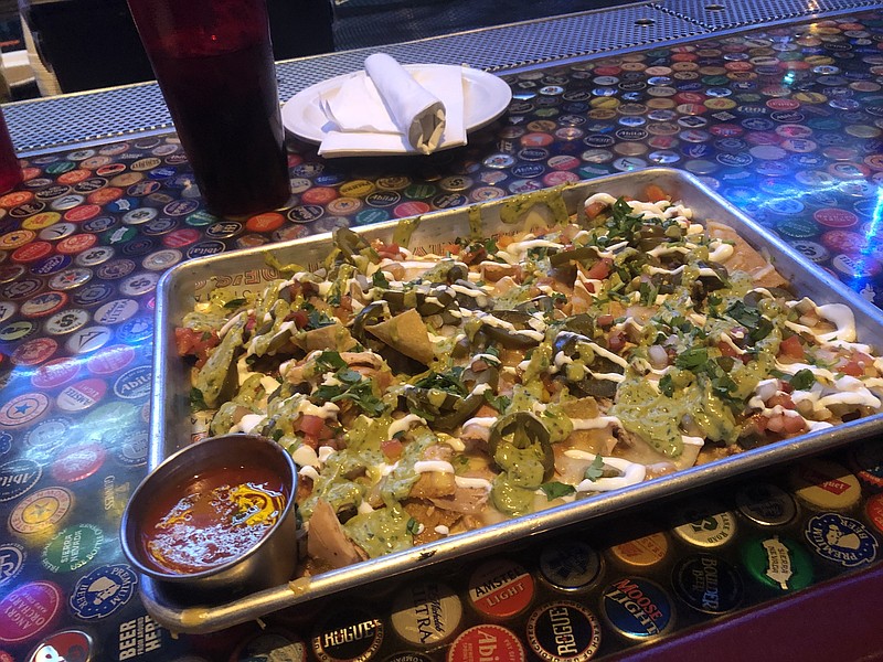 Photo by Jim Tanner / Smoked chicken chili nachos ($12) starts with a pan of pulled smoked chicken chili over chips, topped with spicy avocado cream, pico de gallo, chile verde salsa, sour cream, jalapeno and pepper jack cheese.