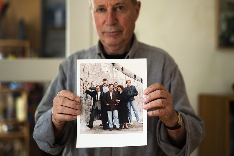 In this Oct. 31, 2019 photo Frieder Reimold the former Berlin bureau chief of The Associated Press' German service shows an undated photo from late 1989 or early 1990 showing the staff of the Associated Press German service Berlin offices, in his house in Stansdorf near Berlin. Frieder Reimold was the AP staffer who sent out the iconic AP news alert, "DDR oeffnet Grenze," or "East Germany opens border" that further accelerated events that night. Then people of the photo are from left: buero chief Frieder Reimhold, West Berlin based correspondent Juergen Mettermeyer, East Berlin based correspondent Ingowerner Schmelz, West Berlin based correspondent Annette Ramelsberger, East Berlin office assistant Barbara Knuth and West Berlin office assistant Annette Kreis.(AP Photo/Markus Schreiber)