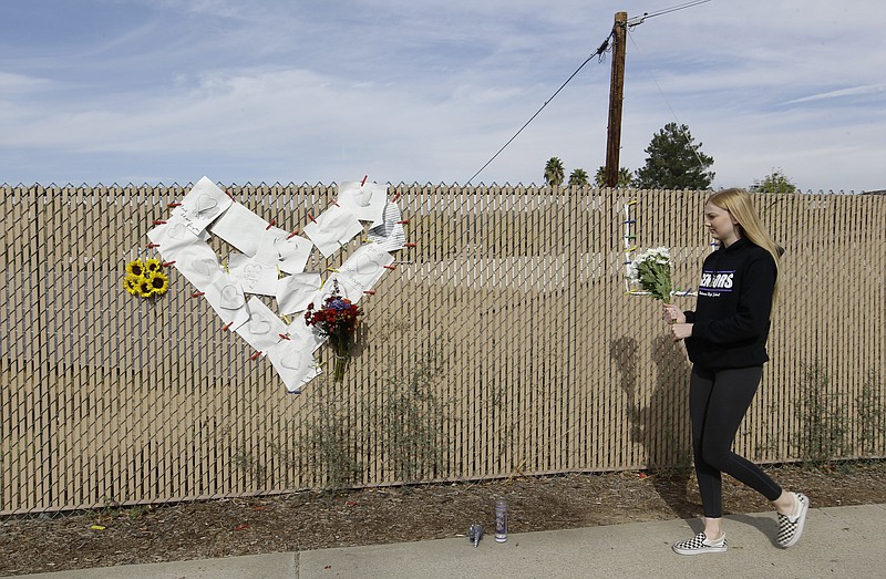 Emily Boyle, a senior at Valencia High School brings flowers at a memorial near Saugus High School in Santa Clarita, Calif., Friday, Nov. 15, 2019. A homicide official says that investigators did not find a diary, manifesto or note belonging to the boy who killed two people outside his Southern California high school on his 16th birthday. Officials held a press conference Friday outside of the police station Santa Clarita. No motive or rationale has been established yet in the Thursday morning shooting at Saugus High School in the Los Angeles suburb of Santa Clarita. (AP Photo/Damian Dovarganes)