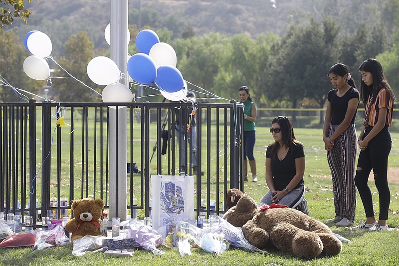 Parent Mirna Herrera kneels with her daughters Liliana, 15, and Alexandra, 16 at the Central Park memorial for the Saugus High School victims in Santa Clarita, Calif., Friday, Nov. 15, 2019. Investigators said Friday they have yet to find a diary, manifesto or note that would explain why a boy killed two students outside his Southern California high school on his 16th birthday. (AP Photo/Damian Dovarganes)