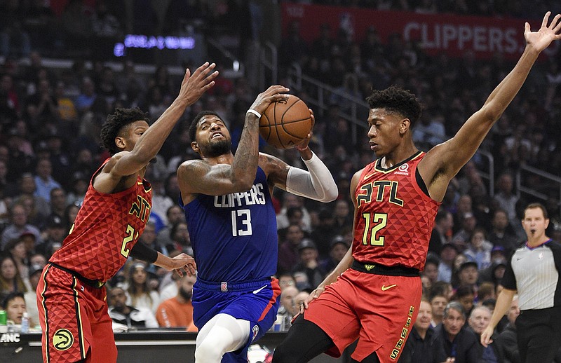 AP photo by Kelvin Kuo / Los Angeles Clippers forward Paul George, center, drives to the basket between Atlanta Hawks forward De'Andre Hunter, right, and forward Cam Reddish during the first half of Saturday night's game in Los Angeles.