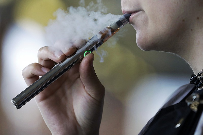 FILE - In this Oct. 4, 2019, file photo, a woman using an electronic cigarette exhales in Mayfield Heights, Ohio. With one in four teenagers now using e-cigarettes, underage vaping is universally condemned, and the federal government considers it an epidemic. But some other researchers believe recent trends continue to show vaping’s promise as a tool to steer millions of adult smokers away from cigarettes, the nation’s leading cause of death. (AP Photo/Tony Dejak, File)