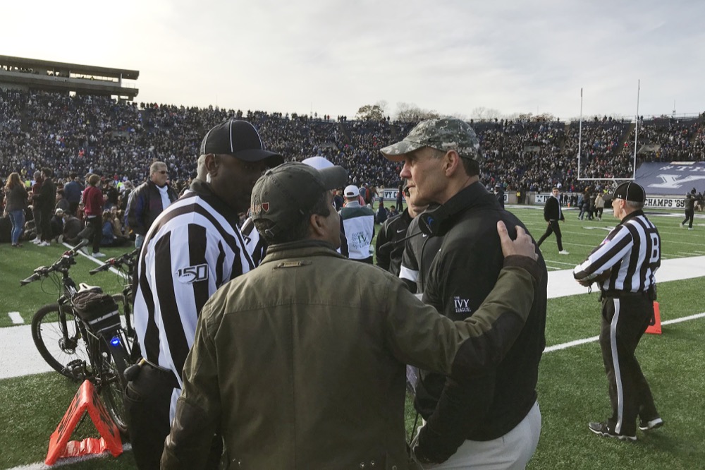 Harvard coach Tim Murphy, right, gets an updated as demonstrators stage a protest on the field at the Yale Bowl disrupting the start of the second half of an NCAA college football game between Harvard and Yale, Saturday, Nov. 23, 2019, in in New Haven, Conn. (AP Photo/Jimmy Golen)