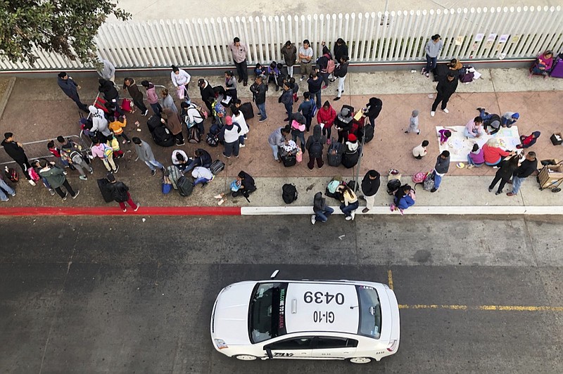 In this Nov. 10, 2019, photo, migrants gather at the U.S.-Mexico border in Tijuana, Mexico, to hear names called from a waiting list to claim asylum in the U.S. (AP Photo/Elliot Spagat)

