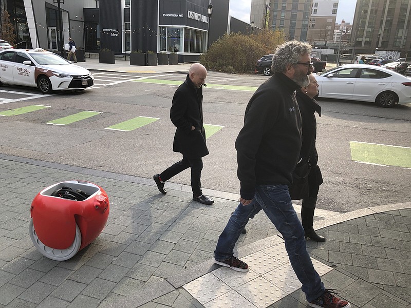 Piaggio Fast Forward CEO Greg Lynn, center, is followed by his company's Gita carrier robot as he crosses a street on Monday, Nov. 11, in Boston. The two-wheeled machine is carrying a backpack and uses cameras and sensors to track its owner. (AP Photo / Matt O'Brien)