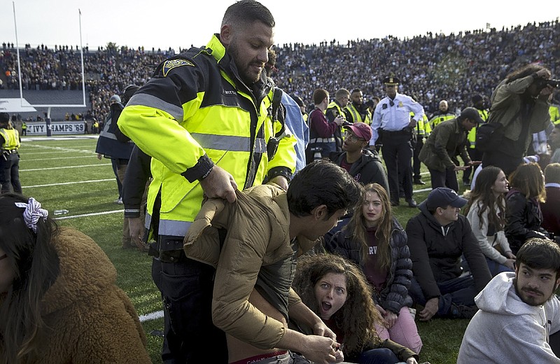 In this Saturday, Nov. 23, 2019, photo, an officer lifts a student up during a protest during halftime of the NCAA college football game between Harvard and Yale at the Yale Bowl in New Haven, Conn. Officials say 42 people were charged with disorderly conduct after the protest interrupted the game. (Nic Antaya/The Boston Globe via AP)