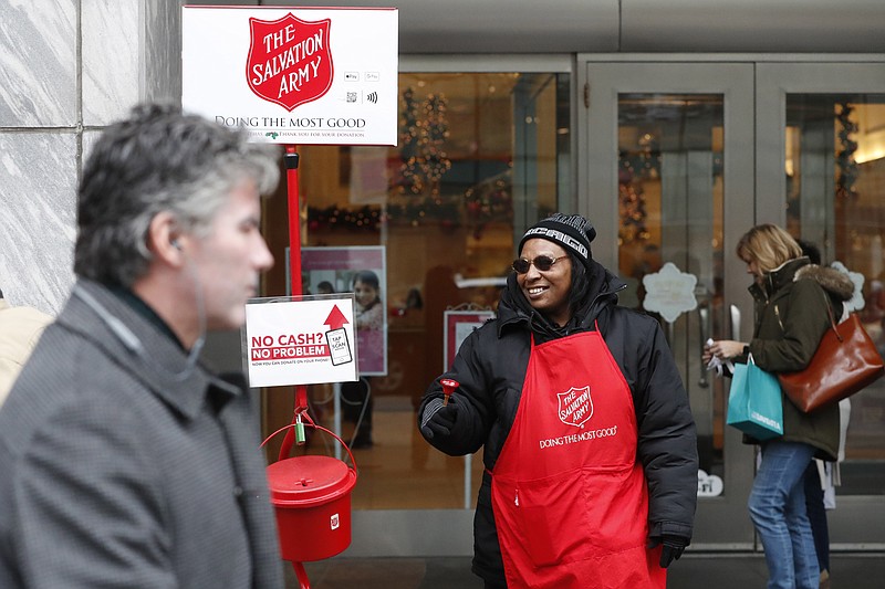 In this Friday, Nov. 15, 2019, photo, bell ringer Carolyn Harper encourages people to donate to the Salvation Army's annual holiday red kettle campaign on Chicago's Magnificent Mile. Cashless shoppers have a new option to give to the Army's red kettle campaign this year using their smartphone. Leaders hope adding Apple and Google payment options will boost fundraising to the campaign, which makes up 10% of The Salvation Army's annual budget. Those donations fund programs providing housing, food and other support to people in poverty. (AP Photo/Charles Rex Arbogast)