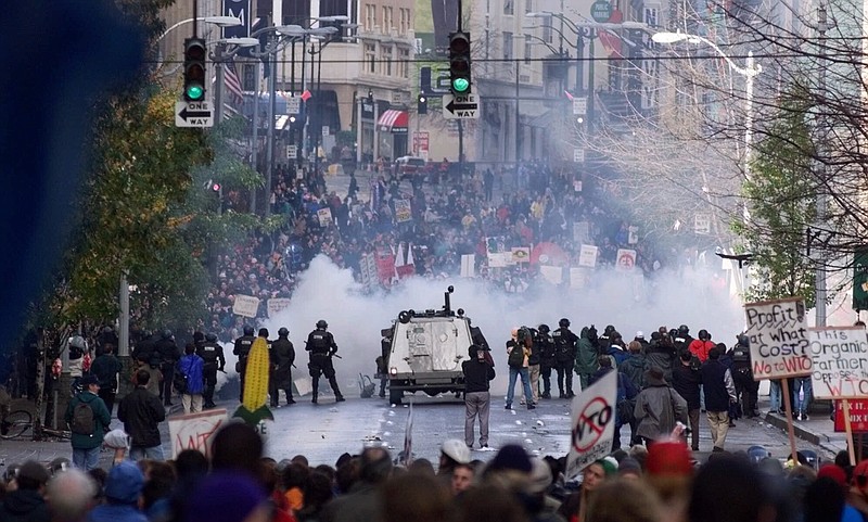 FILE - In this Nov. 30 1999, file photo, Seattle police use tear gas to push back World Trade Organization protesters in downtown Seattle. Saturday, Nov. 30, 2019 marks 20 years since tens of thousands of protesters converged on Seattle and disrupted a major meeting of the World Trade Organization. The protesters' message was amplified not just by their vast numbers but by the response of overwhelmed police, who fired tear gas and plastic bullets and arrested nearly 600 people. Two decades later, many of their causes are still relevant. (AP Photo/Eric Draper, File)