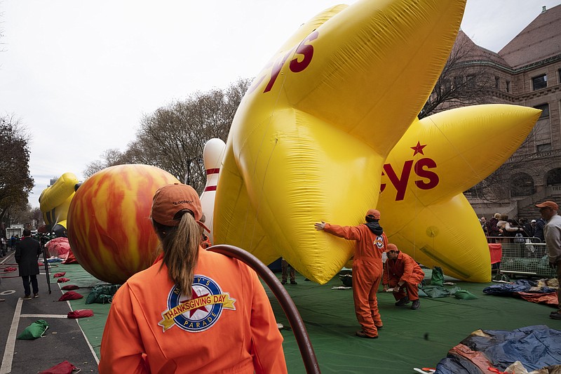 A volunteer shoulders a helium hose as balloons are inflated Wednesday, Nov. 27, 2019, the day before the Macy's Thanksgiving Day Parade in New York. The parade on Thursday will take place amid strong winds that could potentially ground the giant character balloons. (AP Photo/Mark Lennihan)