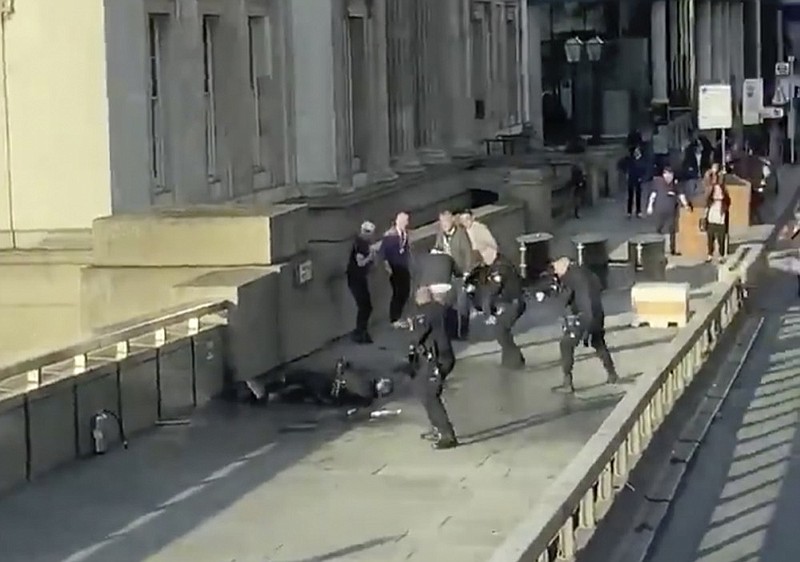 In this grab taken from video made available by @HLOBlog, a man is surrounded by police after an incident on London Bridge, in London, Friday, Nov. 29, 2019. A man wearing a fake explosive vest stabbed several people before being tackled by members of the public and then shot dead by armed officers on London Bridge, police and the city’s mayor say. Police say they are treating it as a terrorist attack. (@HLOBlog via AP)