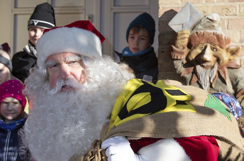 A man dressed as Santa Claus is welcomed by children during the opening of the most famous German Christmas mail office in the small village of Himmelpfort (Heaven's Door) north of Berlin, Germany, Thursday, Nov. 14, 2019. Santa Claus is at it again, answering thousands of Christmas letters from children around the world at a special post office in Himmelpfort. As part of the annual event organized by Germany's Deutsche Post, Santa and 20 helpers last year responded to 277,200 letters from 64 countries. (Soeren Stache/dpa via AP)