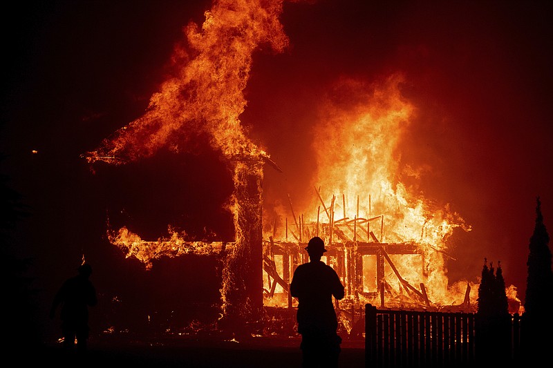 In this Nov. 8, 2018 file photo, a home burns as a wildfire called the Camp Fire rages through Paradise, Calif. Pacific Gas and Electric says it has reached a $13.5 billion settlement that will resolve all major claims related to devastating wildfires blamed on its outdated equipment and negligence. The settlement, which the utility says was reached Friday, Dec. 6, 2019, still requires court approval. (AP Photo/Noah Berger, File)