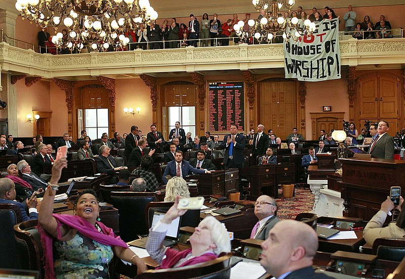 In this April 10, 2019 file photo, some members of the Ohio House applaud following their vote while others photograph protestors who unfurled banners reading "This is not a House of Worship" and "This is not a Doctor's office" following a vote on the Heartbeat Bill at the Ohio Statehouse in Columbus, Ohio. A group of conservative lawmakers in Ohio has introduced a bill to outlaw abortion outright, declaring a fetus a person and subjecting doctors who terminate pregnancies to potential murder charges. The legislation introduced Thursday, Nov. 14, appears to make an exception for the life of the mother.(Brooke LaValley/The Columbus Dispatch via AP, File)