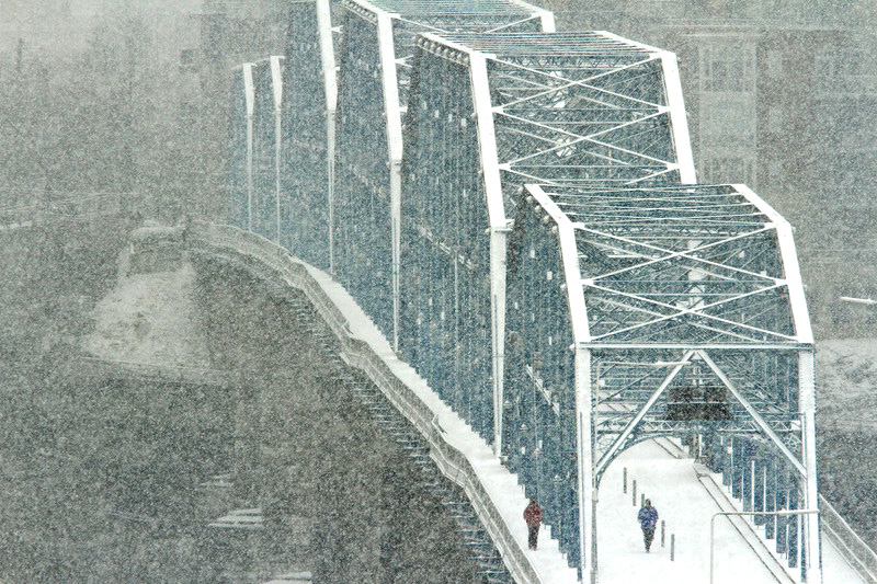 Pedestrians walk across the Walnut Street Bridge as snow accumulates on February 12, 2014.