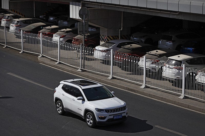 FILE - In this March 14, 2019, file photo, an SUV moves past dust-covered new Toyota cars stored underneath an overpass in Beijing. China's auto sales sank 5.4% in November from a year ago, putting the industry's biggest global market on track to shrink for a second year, an industry group reported Tues, Dec. 10, 2019. Drivers bought just over 2 million SUVs, sedans and minivans, according to the China Association of Automobile Manufacturers.(AP Photo/Andy Wong, File)