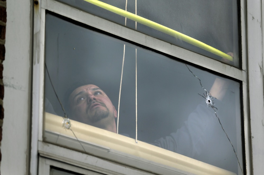 A man measures a window broken by a bullet at the Sacred Heart School, across the street from a kosher supermarket, in Jersey City, N.J., Wednesday, Dec. 11, 2019. The mayor of a New Jersey city says gunmen targeted the kosher market during a shooting that killed six people Tuesday. (AP Photo/Seth Wenig)